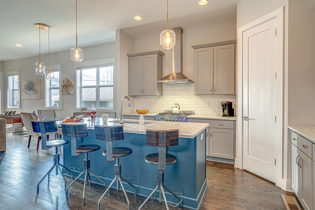 A chic, fully equipped kitchen with a kitchen island and bar stools, modern cabinetry, and elegant lighting. The space is open to living areas and designed for cooking, entertaining, and casual dining.