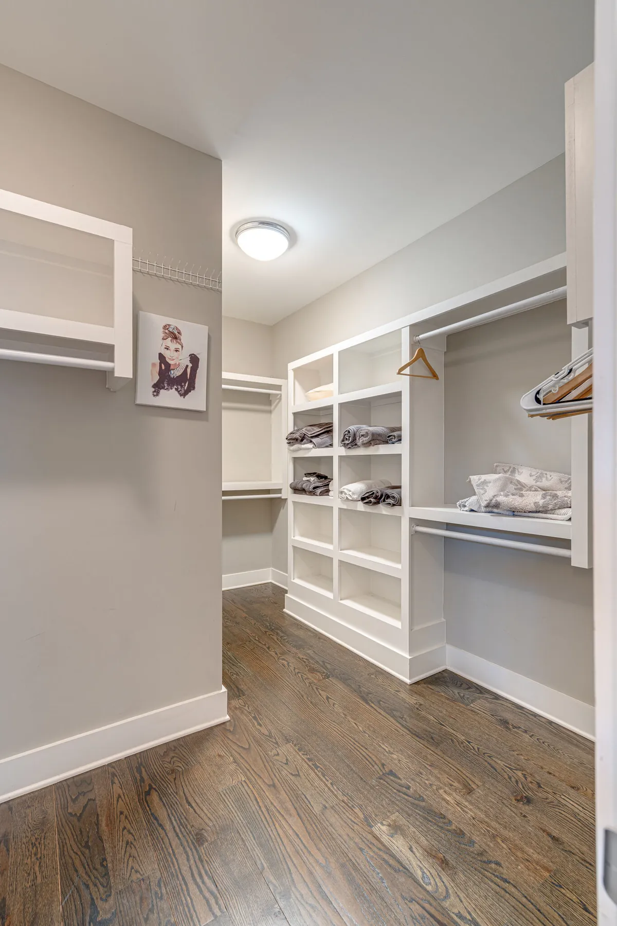 A calm laundry area features neatly organized shelves with linens, a hanging space with hangers, and wall art, creating an orderly and functional environment.