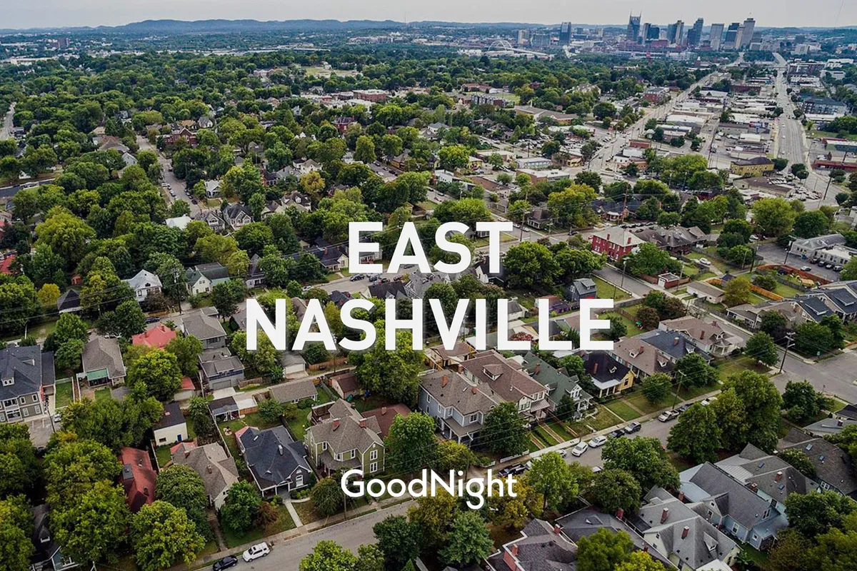 A scenic view featuring residential homes set along lush, tree-lined streets, with the Nashville skyline in the background. The image captures a friendly and vibrant neighborhood atmosphere, ideal for leisurely strolls and pet-friendly walks.
