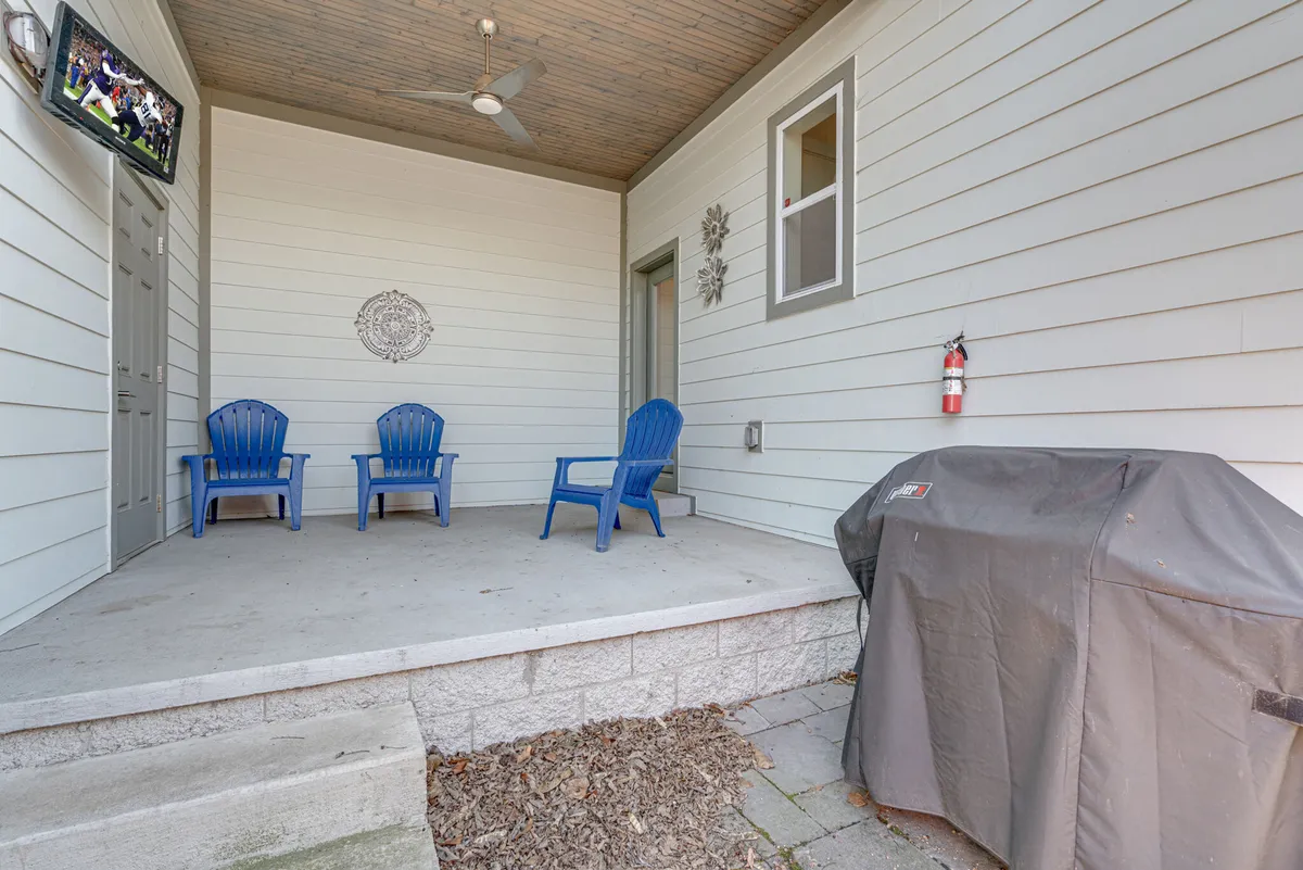 An outdoor patio outfitted with blue chairs, a BBQ grill, and a TV, designed for both relaxing and socializing. The setting is casual and welcoming, ideal for al fresco dining or enjoying summer evenings with friends.