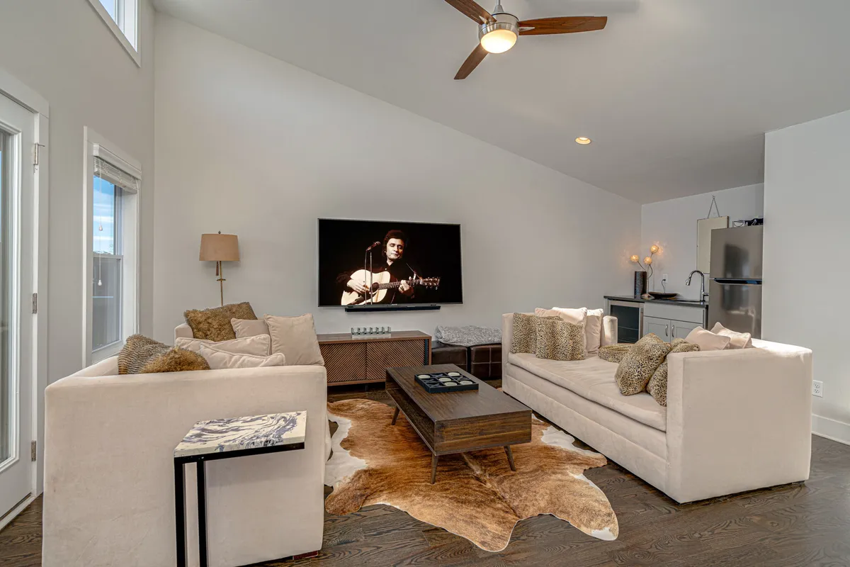 A spacious, modern living room featuring a large TV displaying a musician, a central coffee table, and comfortable sofas arranged for gatherings. The room has an open layout, ideal for socializing, relaxing, or entertainment.