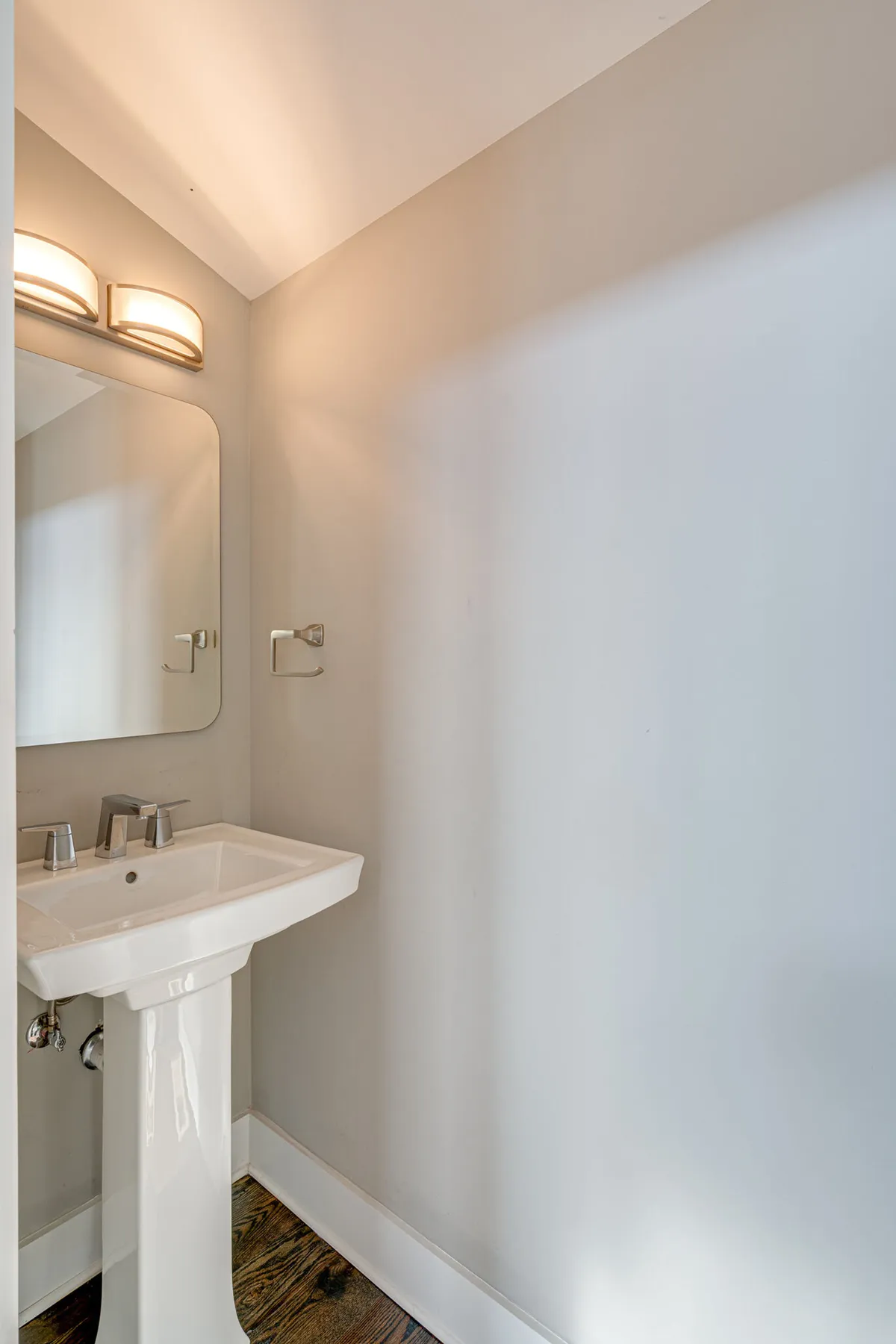 A calm, minimalist bathroom space featuring a clean sink, well-lit mirror, and subtle fixtures. The area feels fresh and organized, reflecting a high degree of cleanliness and attention to detail.