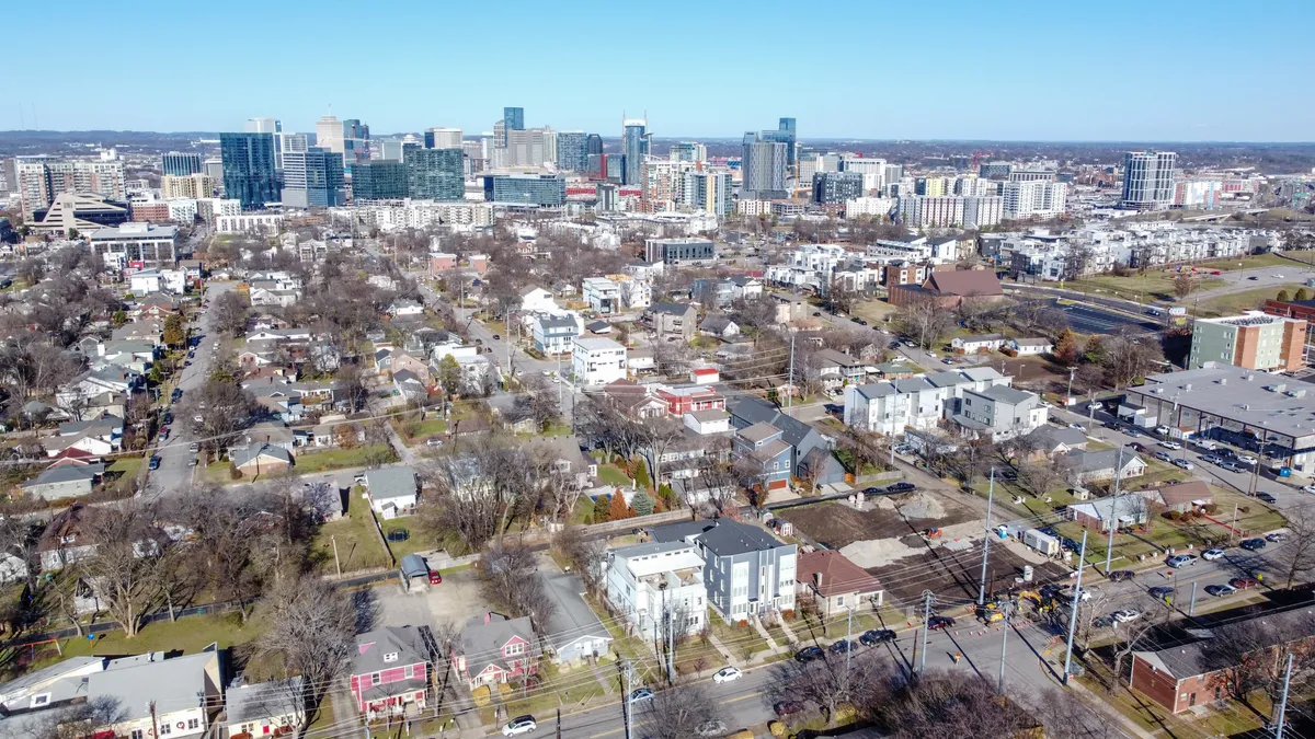 A panoramic view of the city skyline framed by residential neighborhoods, parks, and vibrant roadways. The scene captures the energy of urban life, community events, and outdoor activities, with green spaces inviting groups to gather and explore.