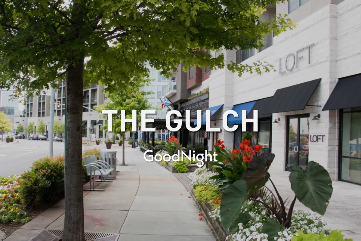 A lively exterior scene showing colorful storefronts, sidewalk seating, and blooming flower beds along a bustling urban street. The atmosphere is welcoming, suggesting a pet-friendly environment where residents and visitors can enjoy shopping, dining, and relaxing outdoors.