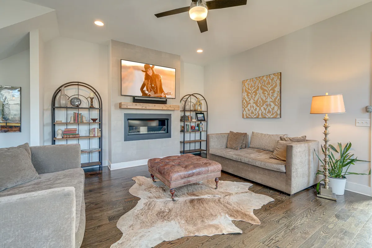 A beautifully styled living room featuring a chic farmhouse design, with a cozy fireplace, inviting coffee table, wall art, shelves lined with books, and soft lighting from a stylish lamp. The space is arranged for both relaxation and social gatherings, offering a warm and welcoming atmosphere.