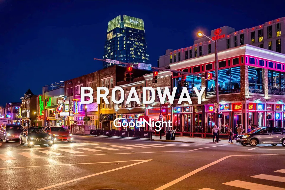 A bustling city street scene at night, filled with neon signs and people strolling past nightlife establishments. The energy is palpable, with live music and dining experiences spilling out onto the sidewalks, capturing Nashville’s famed honky tonk culture.